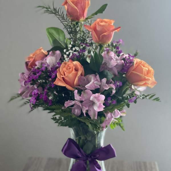 Bouquet of peach roses and purple flowers in a glass vase with a purple ribbon