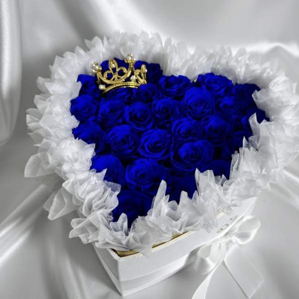 Heart-shaped box of blue roses with white ruffled trim and a gold crown