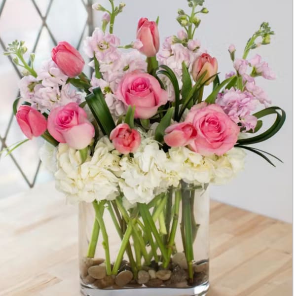 Pink roses and tulips in a clear glass vase with white blooms