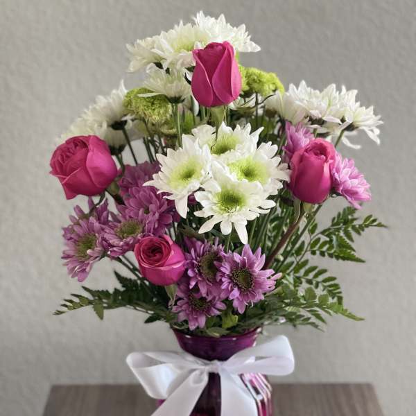 Pink roses and white daisies in a purple vase with a white ribbon