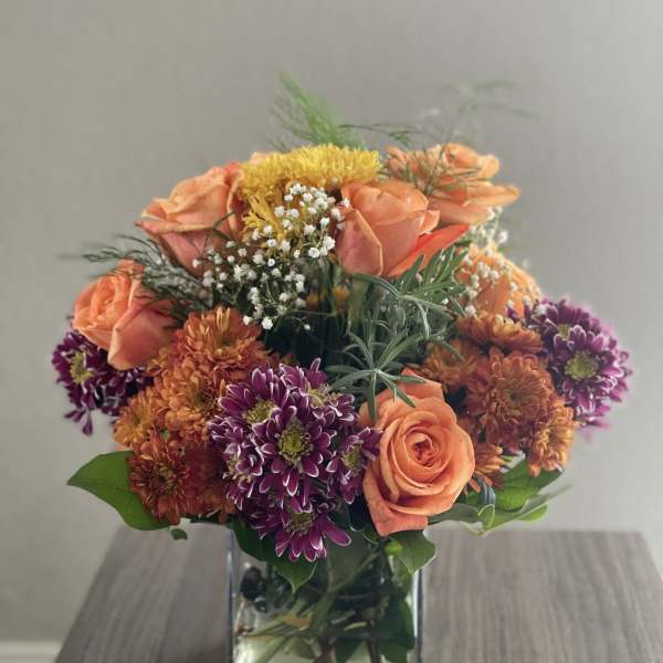 Orange and purple mixed flowers arranged in a square glass vase