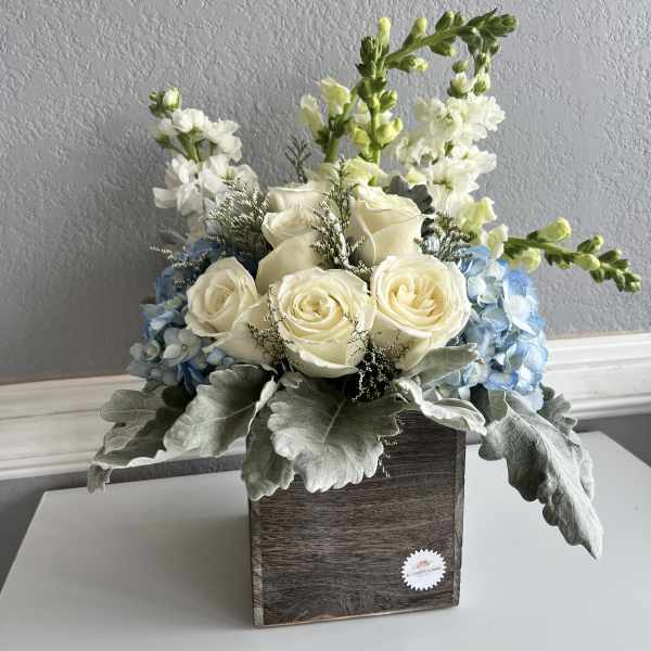 White roses and blue hydrangeas in a wooden box with tall white blooms