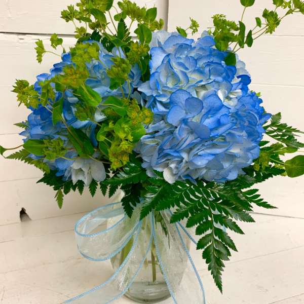 Blue hydrangea bouquet in a glass vase with a light blue ribbon