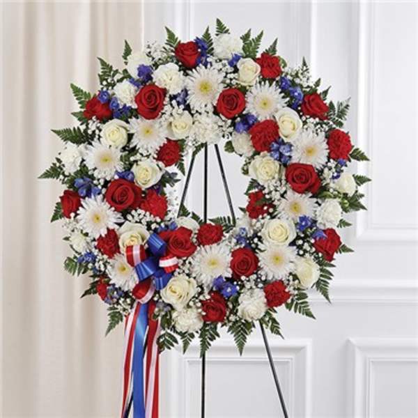 Circular red, white, and blue floral wreath on a stand with ribbon