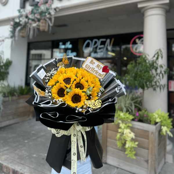 Sunflower bouquet wrapped in black paper with a "Be My Girlfriend" sign