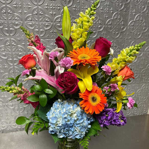 Colorful mixed bouquet in a glass vase with roses, lilies, gerbera daisies, and hydrangea