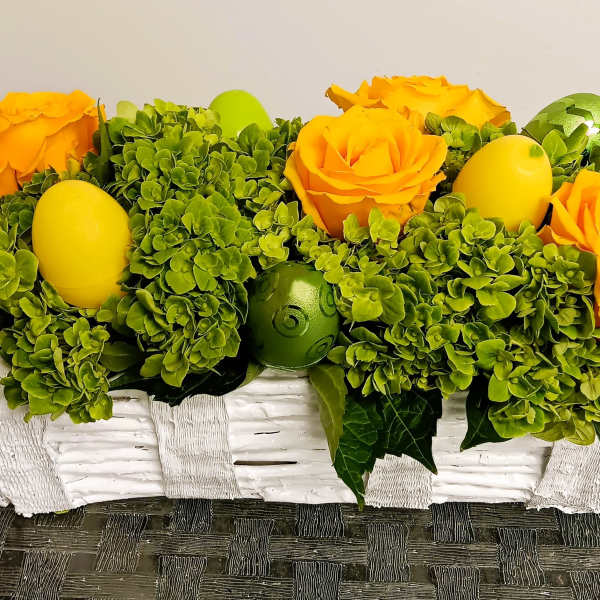 Yellow roses and green hydrangeas in a white basket with decorative eggs