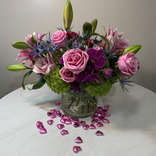 Pink roses and lilies arranged in a glass vase with heart confetti