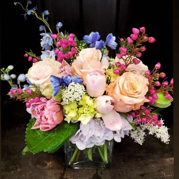 Pastel bouquet of roses, tulips, hydrangea, and blue flowers in a glass vase