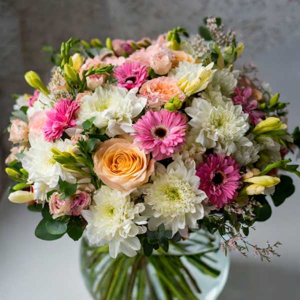 Mixed bouquet of pink, peach, and white flowers in a glass vase