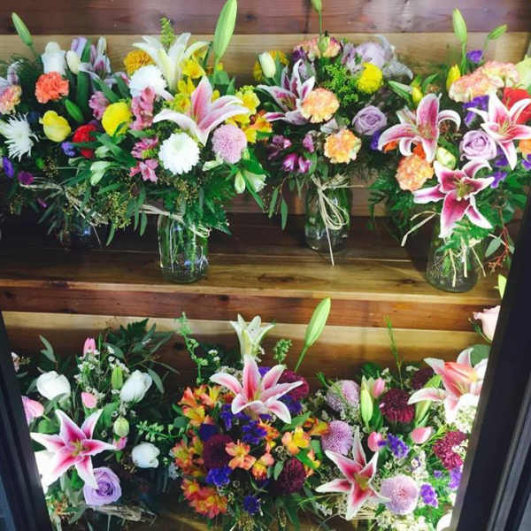 Assorted colorful flower bouquets arranged on wooden shelves in glass jars