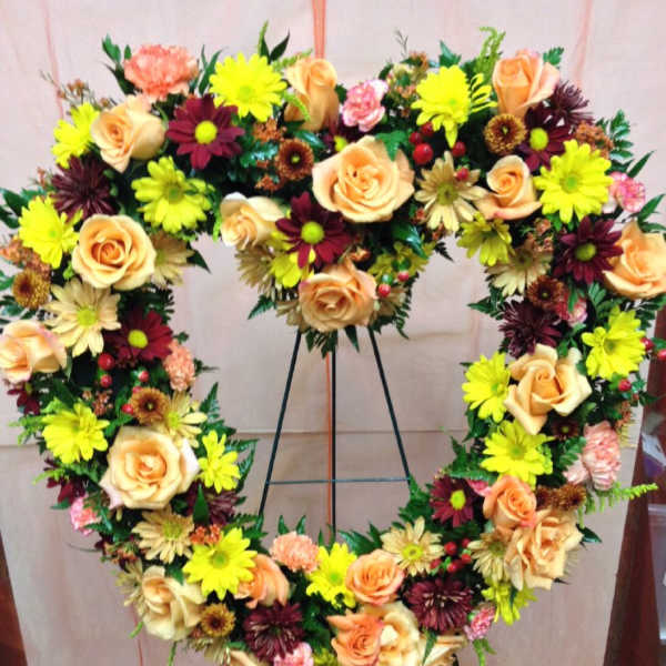 Heart-shaped floral wreath with peach roses and bright daisies on a stand