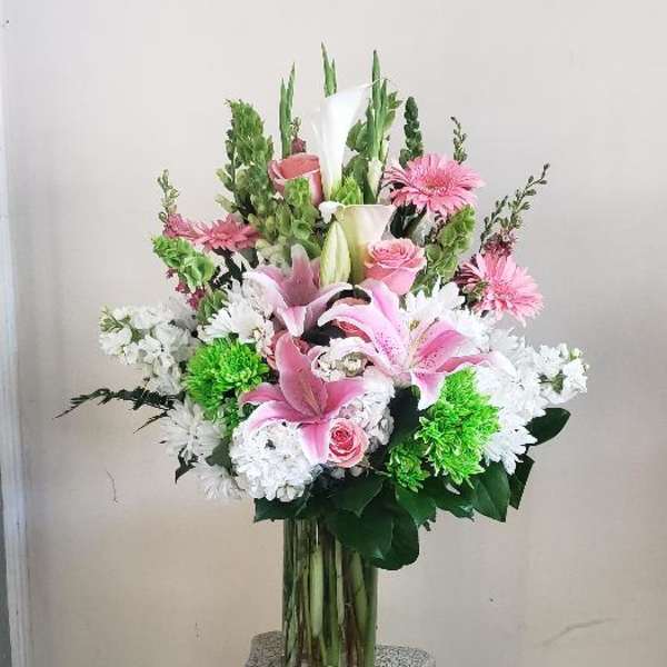Pink lilies and white flowers arranged in a glass vase on a pedestal