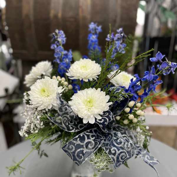 White chrysanthemums and blue flowers in a silver vase with a patterned ribbon