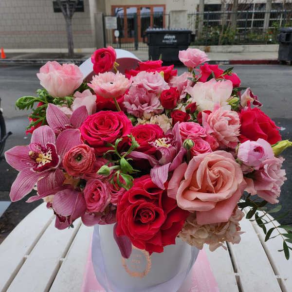 Pink and red mixed flower bouquet in a white hatbox