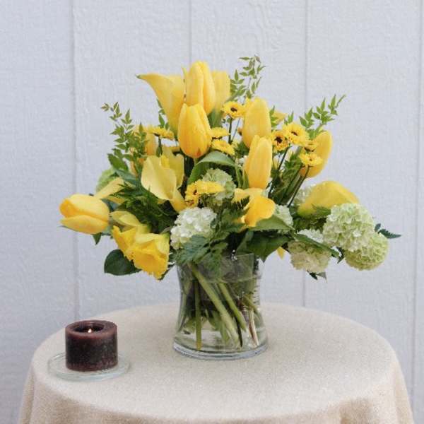 Yellow tulips and white hydrangeas in a clear glass vase beside a candle