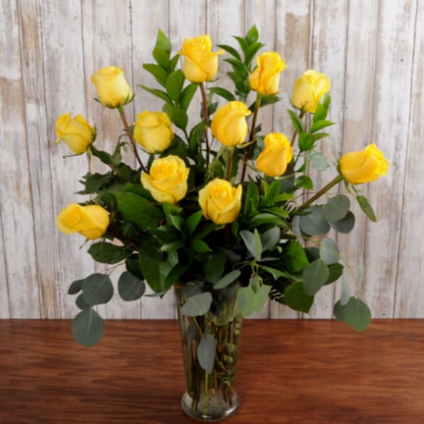 Yellow roses arranged in a clear glass vase with eucalyptus
