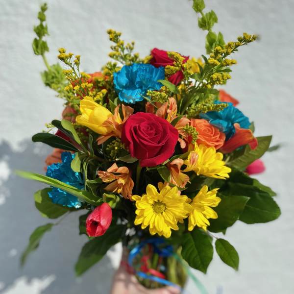 Handheld bouquet of mixed bright flowers in a glass vase