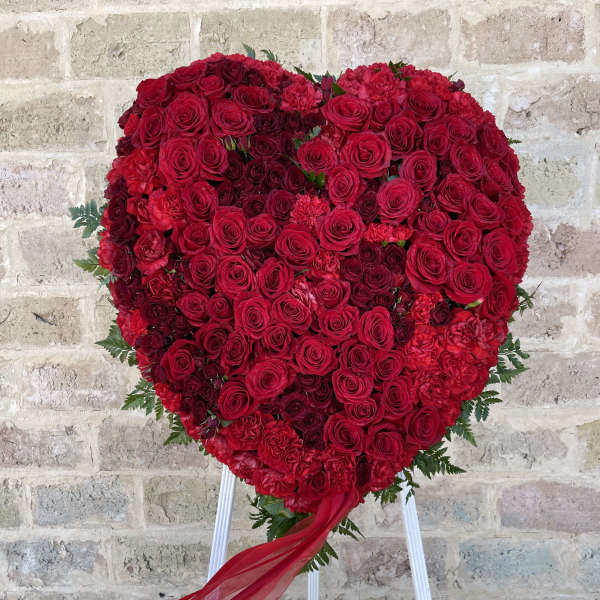 Heart-shaped red rose arrangement on a stand with a flowing ribbon
