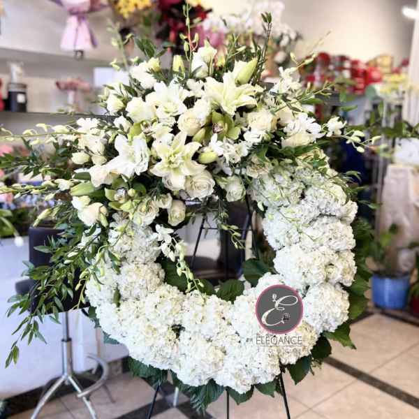 Large white floral wreath on a stand with lilies and roses