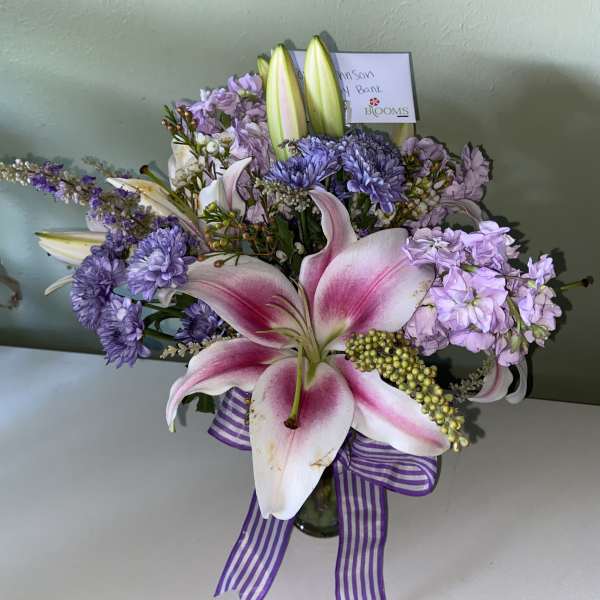 Pink lilies and lavender flowers in a glass vase with a striped ribbon