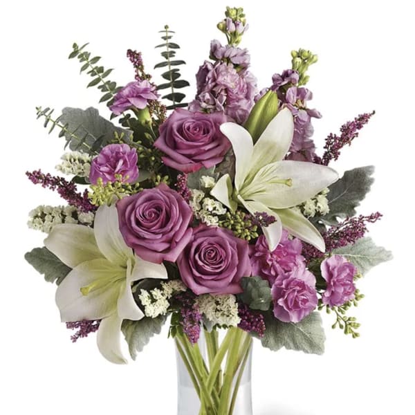 Purple roses and white lilies in a clear glass vase
