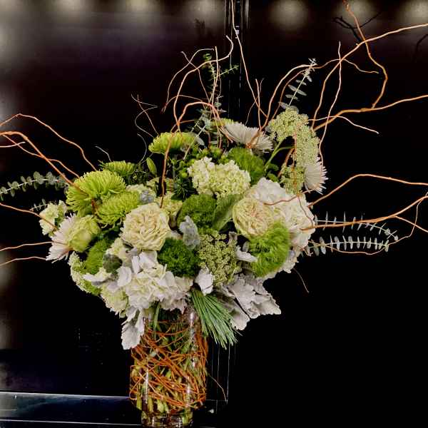 Tall floral arrangement with white and green blooms in a glass vase