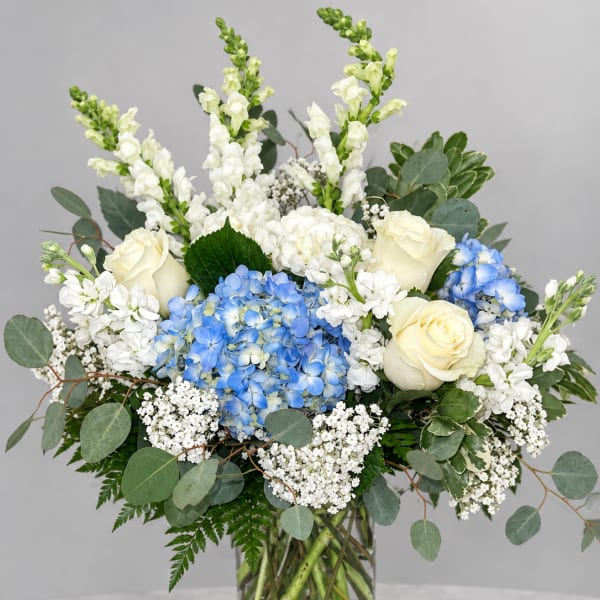 Blue hydrangeas and white roses in a glass vase with mixed greenery