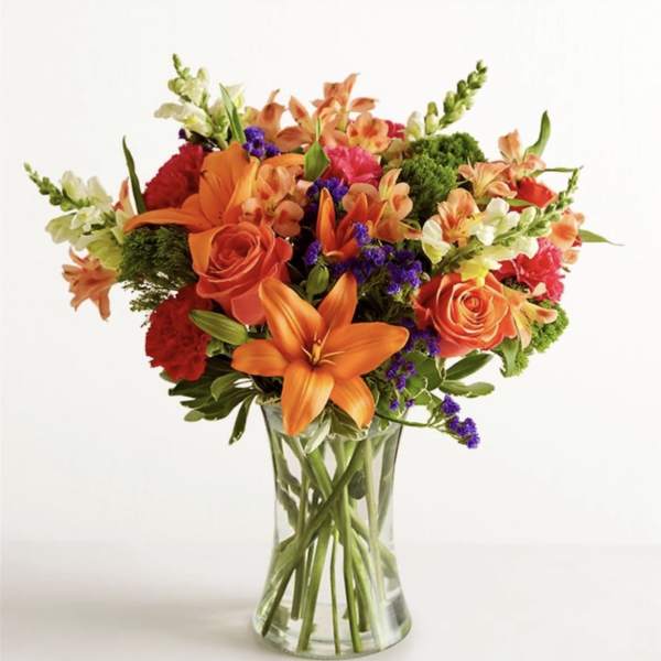 Mixed bouquet of orange and red flowers in a clear glass vase