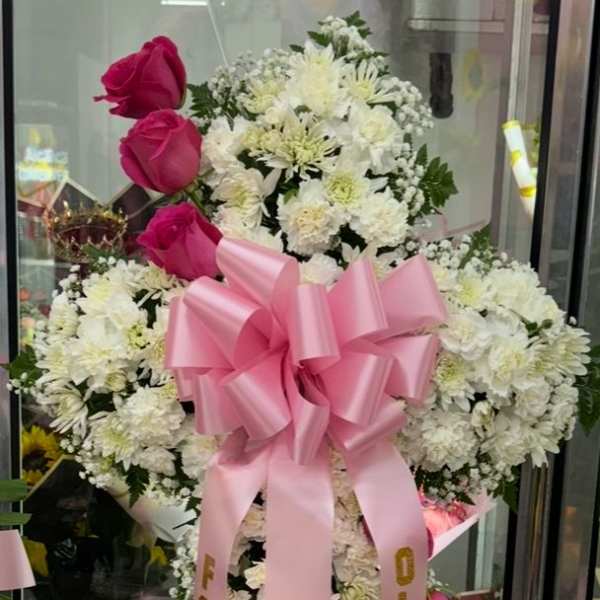 Large white floral standing spray with pink roses and a pink ribbon bow