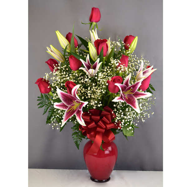 Red roses and pink lilies in a red vase with a ribbon bow
