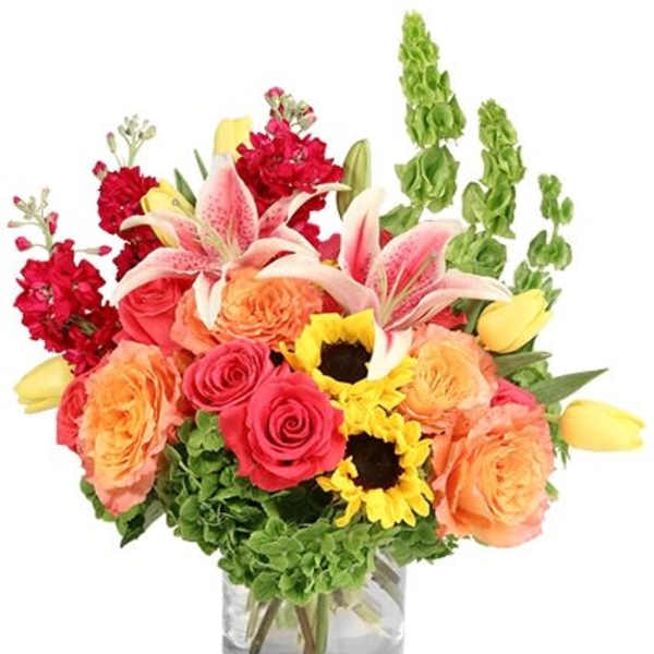 Mixed bouquet of roses, lilies, sunflowers, and red blooms in a glass vase