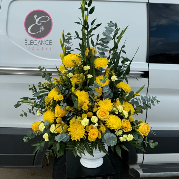 Tall yellow floral arrangement in a white urn vase