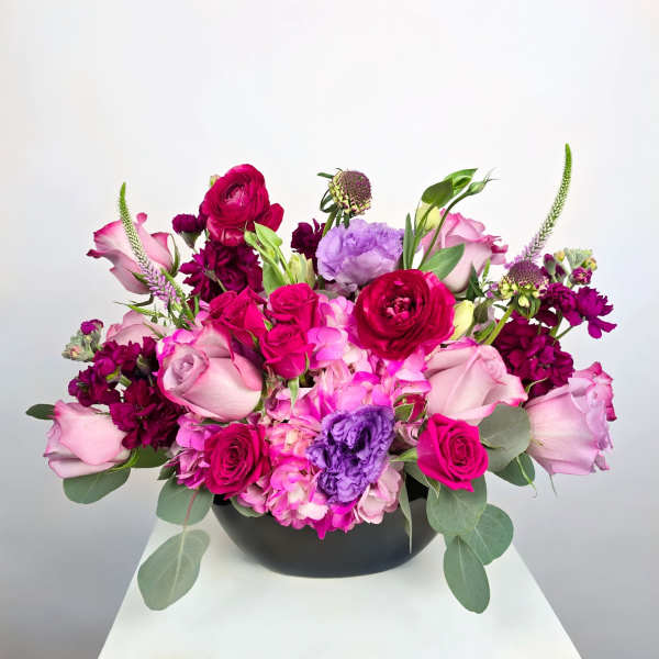 Pink and purple floral arrangement in a black bowl vase
