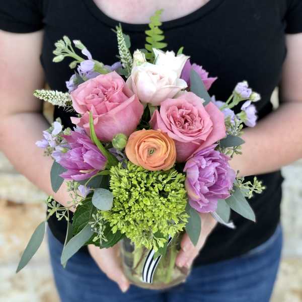 Handheld bouquet of pink, white, purple, and peach flowers in a glass vase