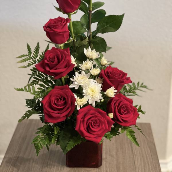 Red roses and white daisies arranged in a square vase