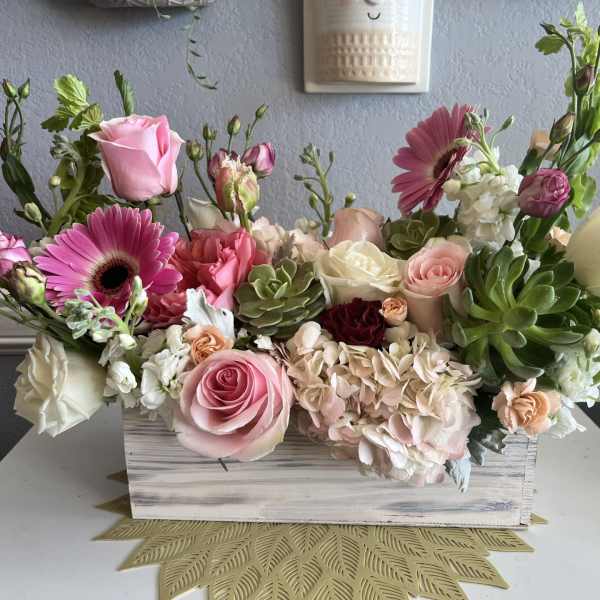 Pink and white floral arrangement in a wooden box with succulents