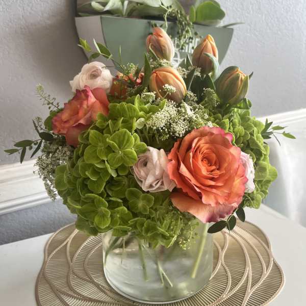 Bouquet of orange roses, green hydrangeas, and tulips in a glass vase