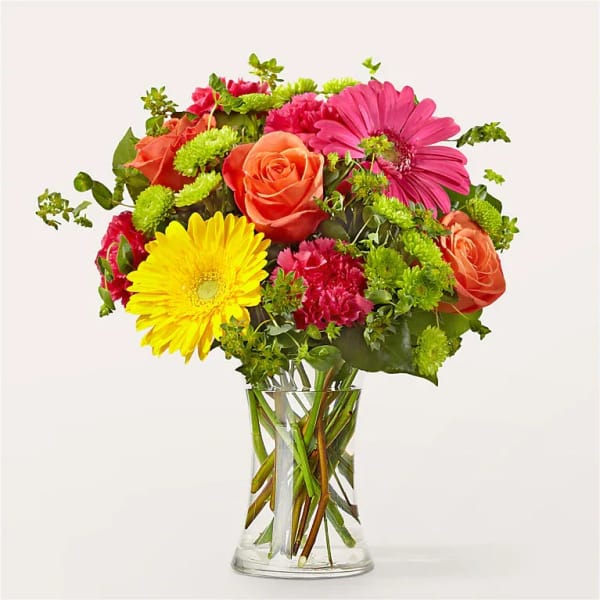 Mixed bouquet of roses, gerbera daisies, and carnations in a clear glass vase