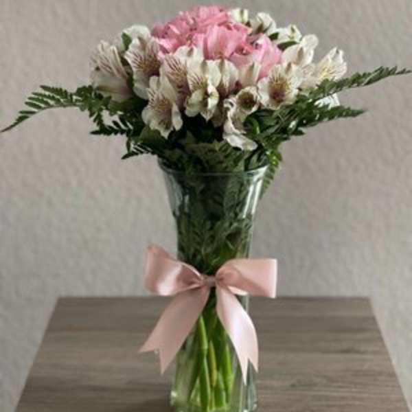 Pink and white bouquet in a clear glass vase with a pink ribbon