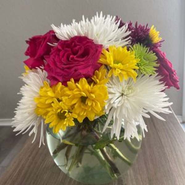 Colorful bouquet of roses and daisies in a round glass vase
