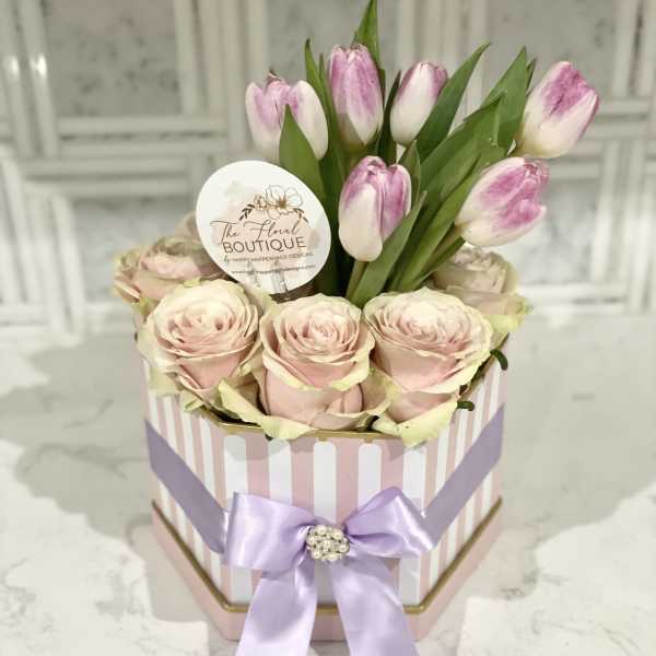 Pink roses and tulips arranged in a striped gift box with a lavender ribbon.