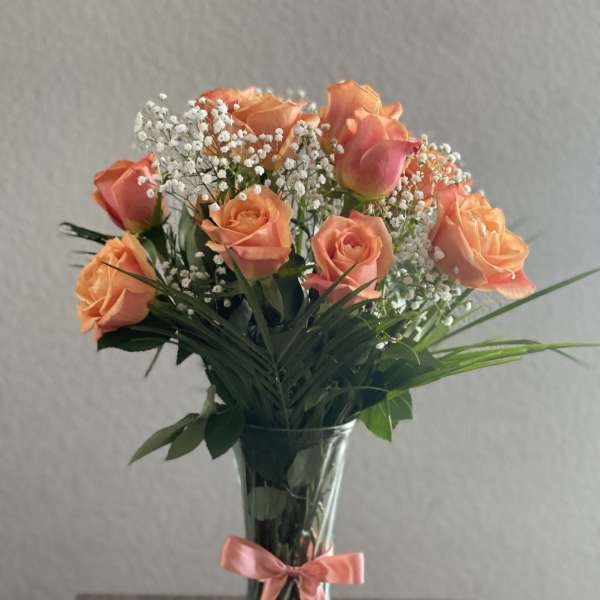Peach roses in a clear glass vase with a pink ribbon