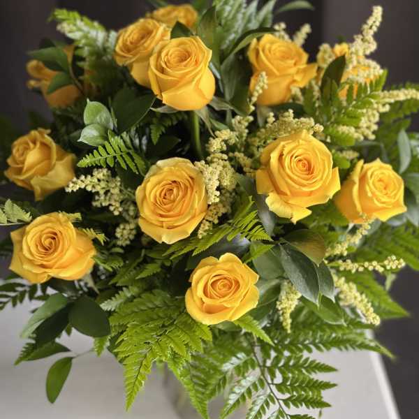 Bouquet of yellow roses with green foliage in a clear vase