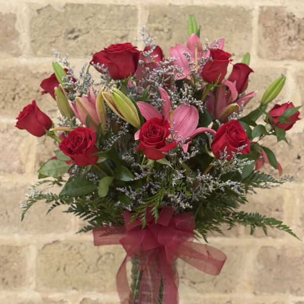 Bouquet of red roses and pink lilies in a glass vase with a ribbon