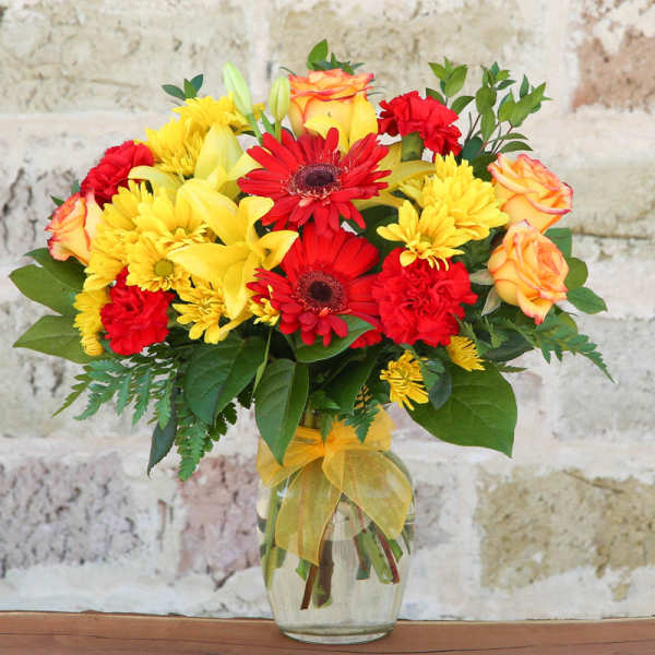 Bouquet of red, yellow, and orange flowers in a glass vase with a yellow ribbon