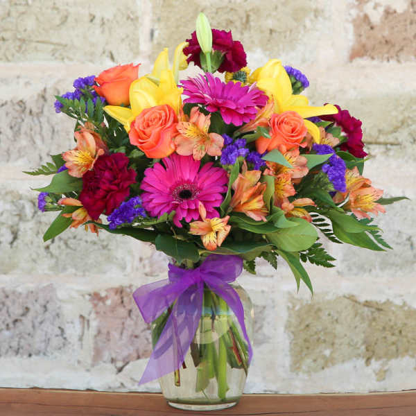 Colorful mixed bouquet in a glass vase with a purple ribbon