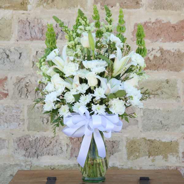 White floral arrangement in a glass vase with a white ribbon