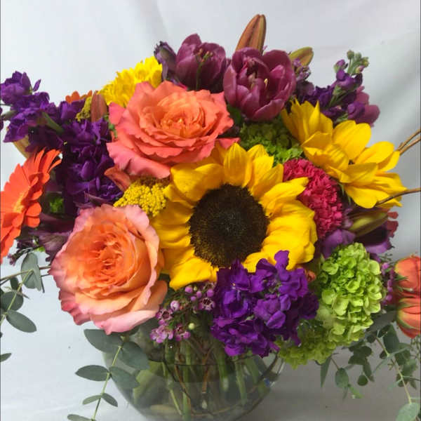 Colorful bouquet with sunflowers, peach roses, and purple blooms in a glass vase