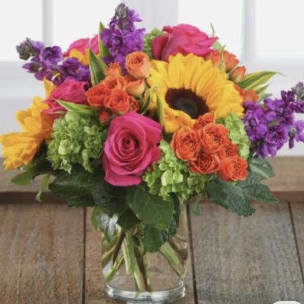 Colorful bouquet of roses, sunflowers, and purple flowers in a glass vase